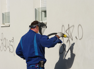 Mann entfernt mit Trockeneisstrahlgerät eine mit Grafitti beschmierte Wand